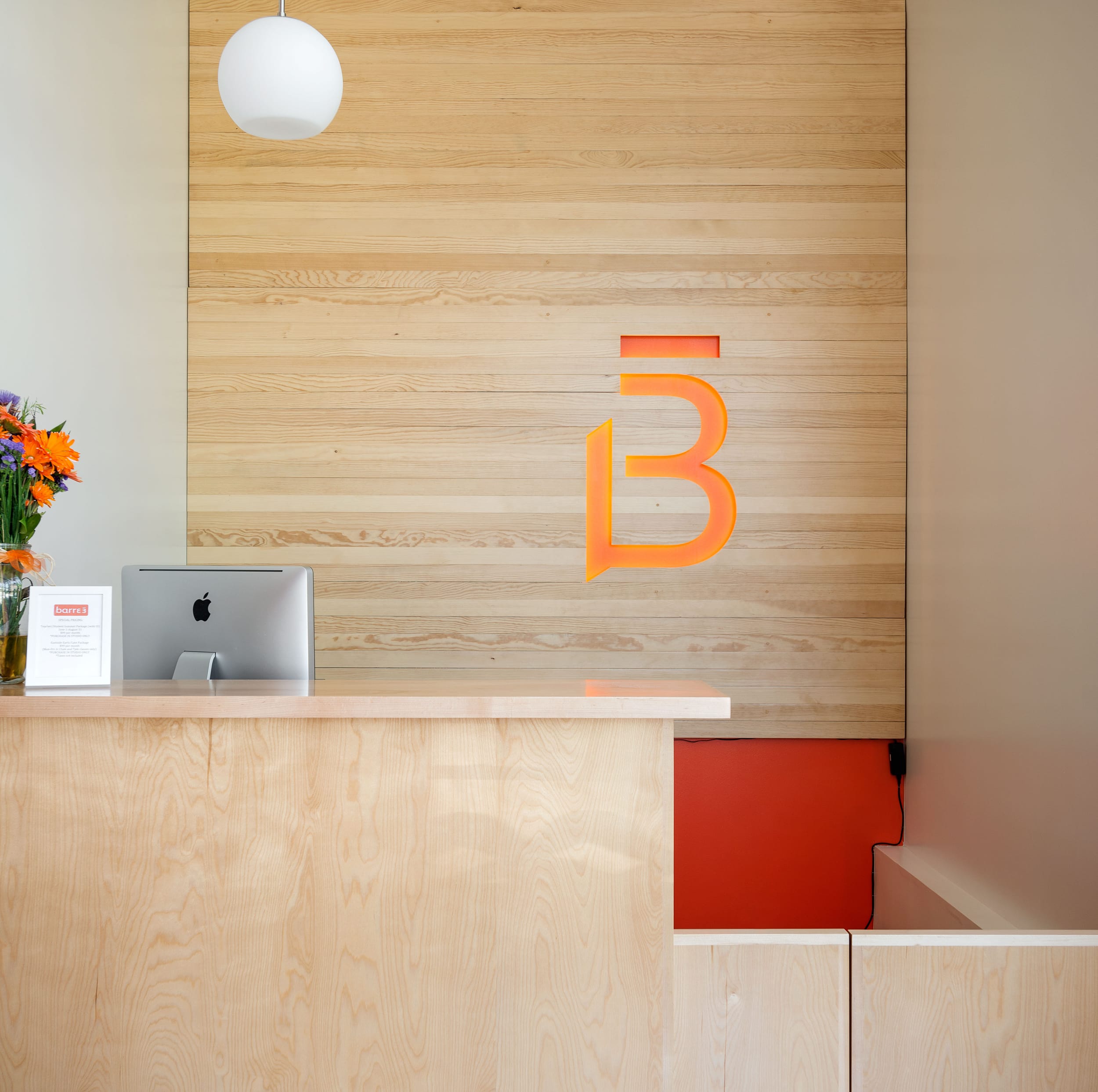 A reception desk with a computer and a vase of flowers.