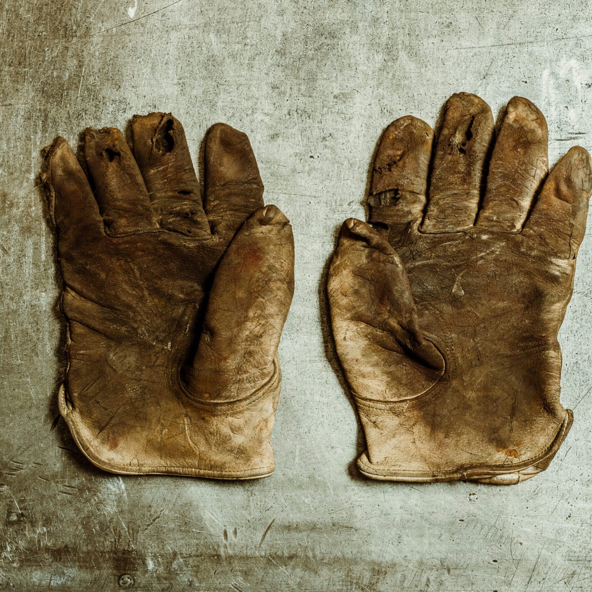 A pair of worn, dirty work gloves lie flat on a scratched metal surface at Dyna Metal Shop Seattle.