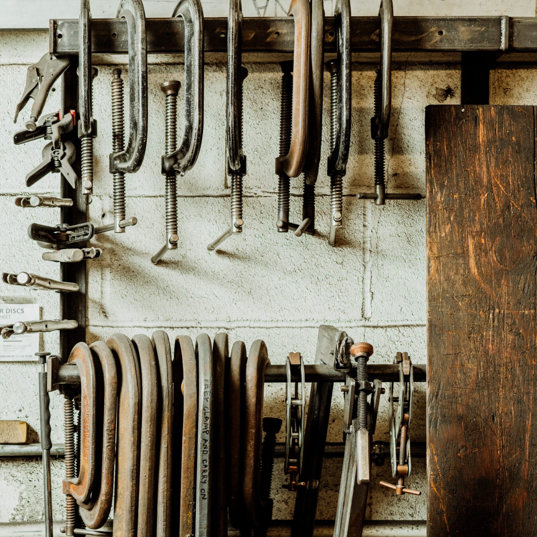 Metal clamps of various sizes hang on racks against a white brick wall in the Dyna Metal Shop Seattle workshop.
