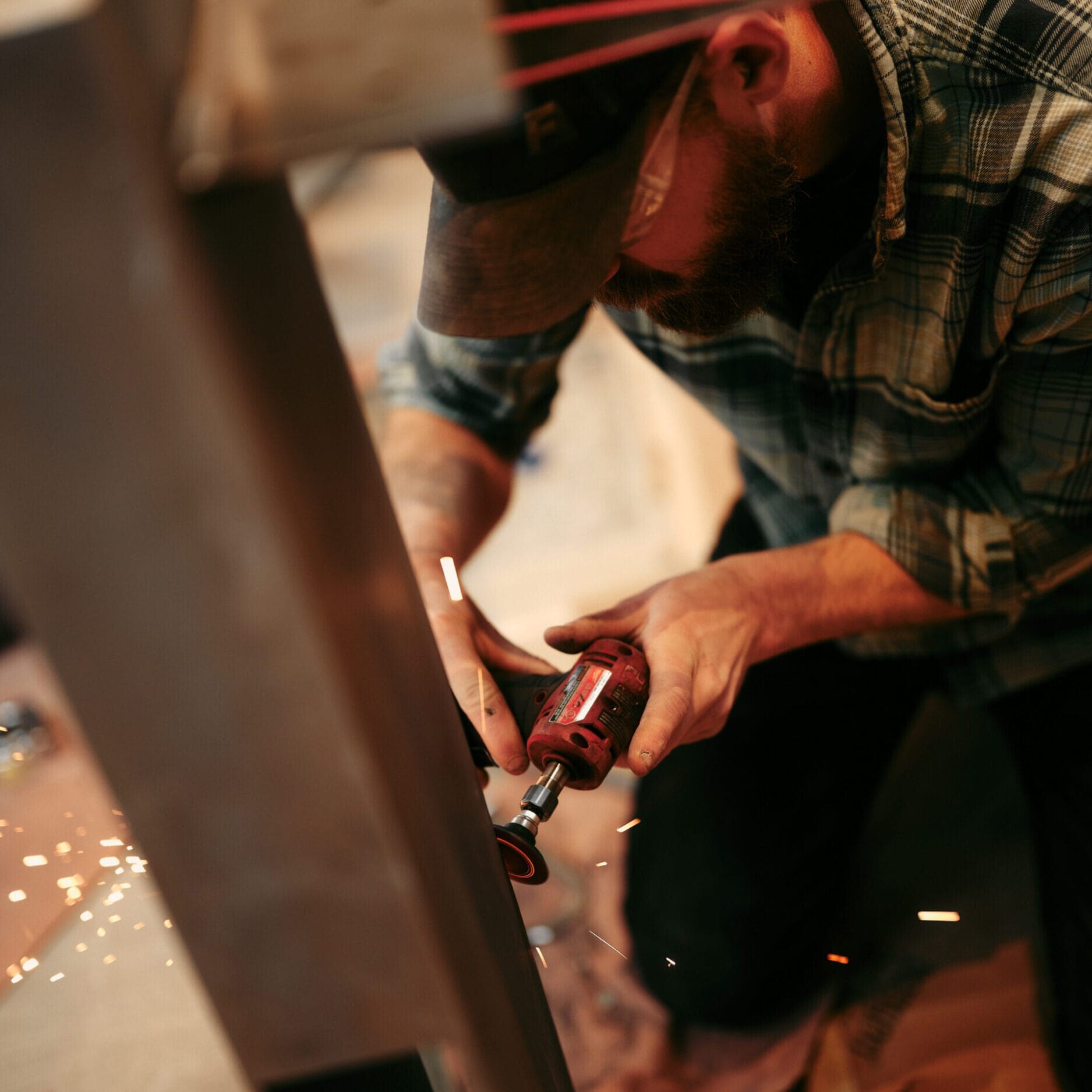 A person wearing a plaid shirt uses a power tool to grind or cut metal, sending sparks flying inside Dyna Builders Metal Shop in Seattle.