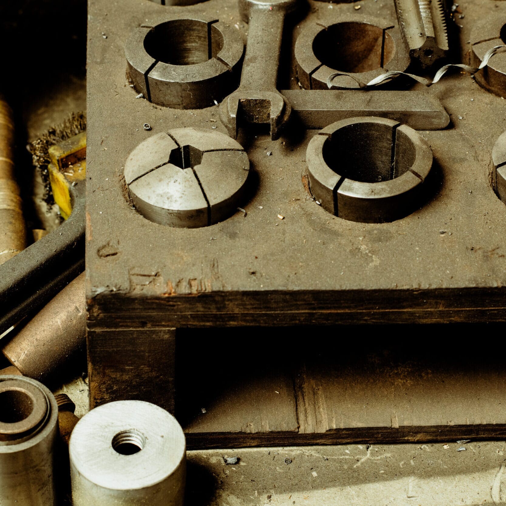A set of metal machine parts and collets arranged on a dusty workbench in the Dyna Metal Shop Seattle workshop.