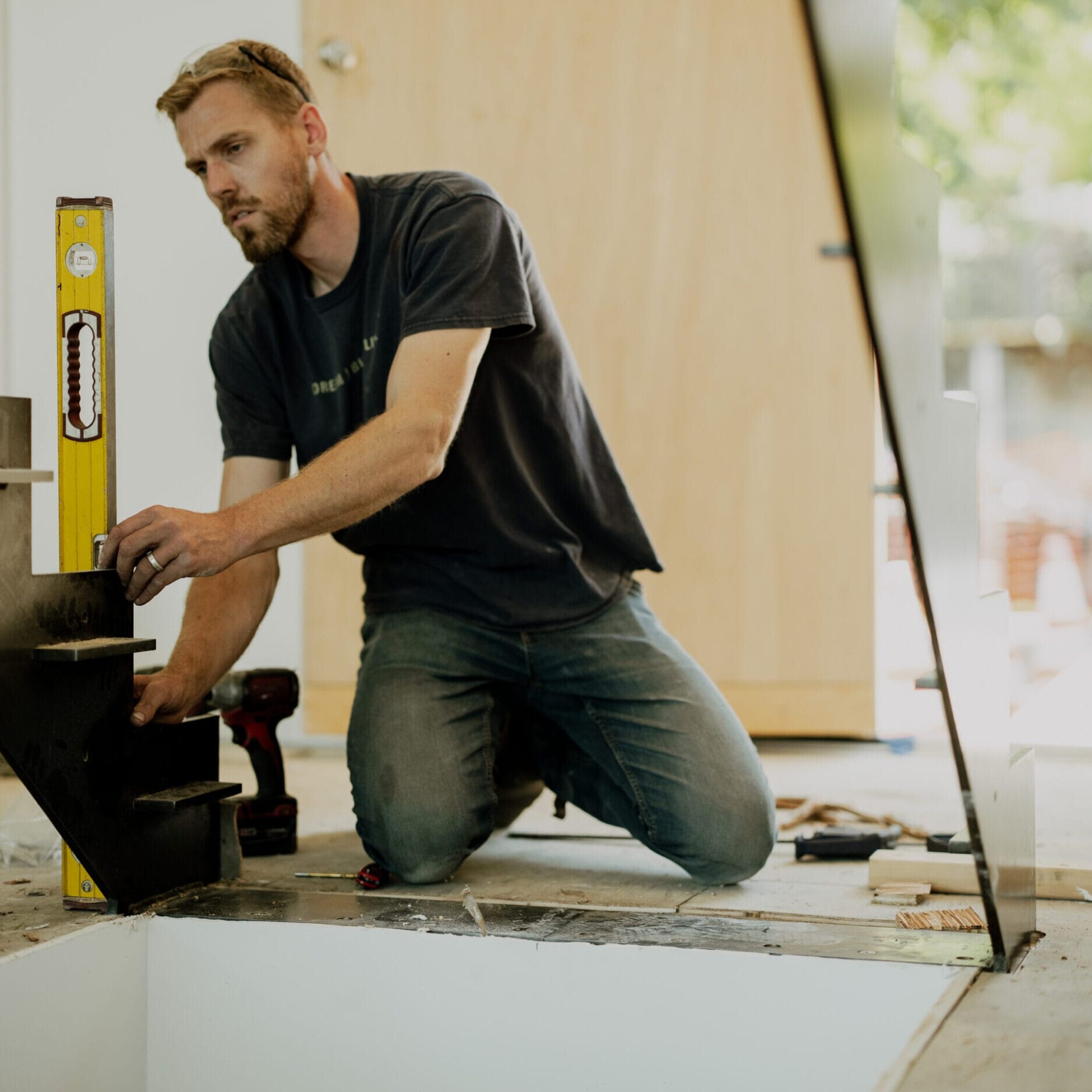 A man kneeling indoors uses a spirit level tool to check the alignment of a metal staircase under construction at Dyna Builders Metal Shop.